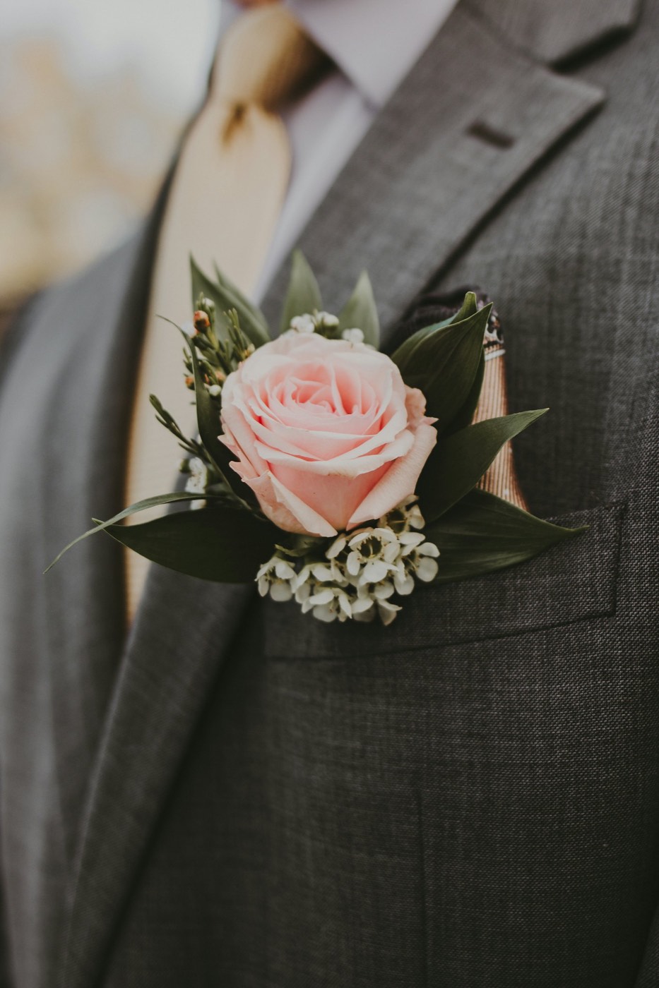 A blush rose boutonniere pinned to a grey lapel